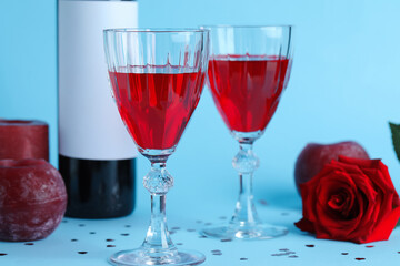Glasses of wine, bottle and rose flower on blue background. Valentine's Day celebration
