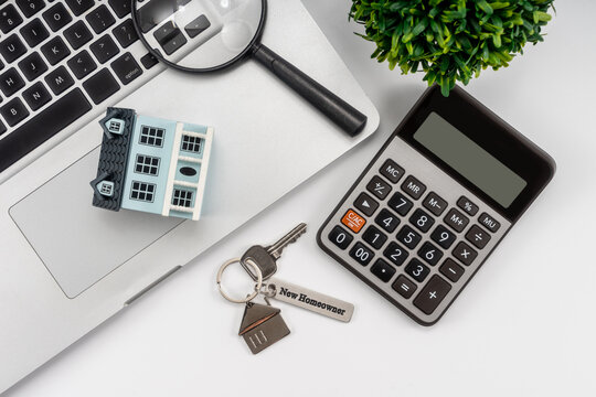 Classic house model, house key with "new homeowner", laptop, Magnifying glass, calculator and pen on white background.