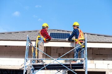A team of Asian technicians installs solar panels on the roof of a house. Cross-section view of builder in helmet installing solar panel system concept of renewable energy