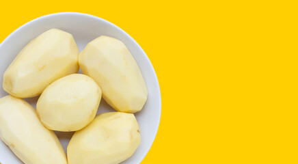 Raw peeled potatoes in white plate on yellow background.