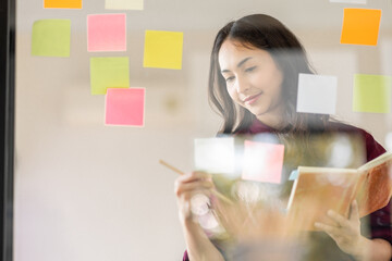Business female employee with many conflicting priorities arranging sticky notes commenting and brainstorming on work priorities colleague in a modern office.
