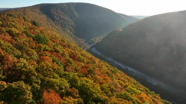 Dramatic aerial flight among mountaintop in autumn. Valley and river below. Fog clouds pass by.