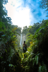 young hiker admiring a mountain waterfall surrounded by vegetation in the middle of the tropical...