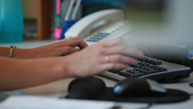 Female hands at workplace desk typing on keyboard and writing in notebook