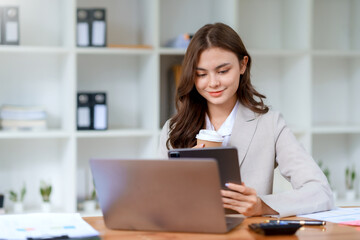 Young beautiful Asian businesswoman working with laptop computer and checking important documents in office, smiling and happy at work.