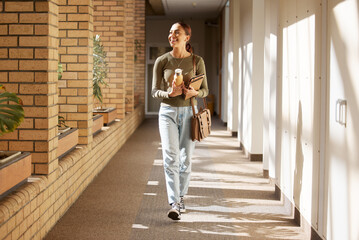 Woman, student and university hallway with a person walking ready for learning and study. Smile,...