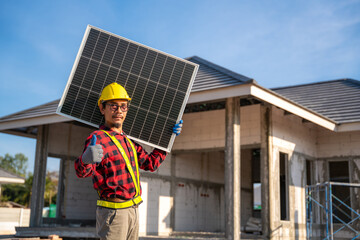 Asian technician holding solar panel with thumbs up showing confidence in front of unfinished house at construction site. Concept of alternative and renewable energy.
