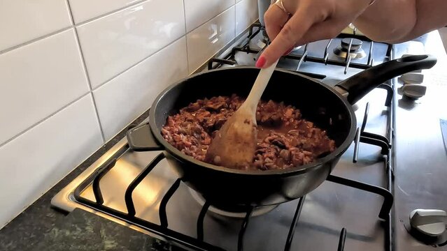 Woman stirring chicken livers on a gas stove top to make chicken liver pate