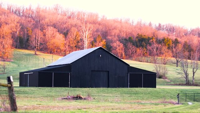 Still image of a black barn at the base of a hillside covered with fall foliage in Kentucky.