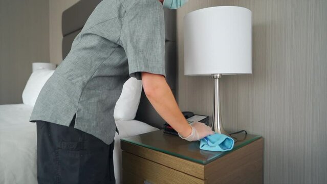 The maid efficiently goes about her tasks, tidying up the hotel room with precision and care, by wiping and cleaning everything in a hotel room.