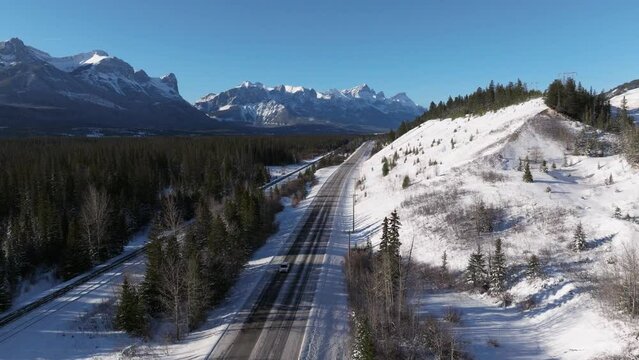 Car drives alone on Bow Valley Trail highway in Canmore Alberta during winter with Mount Rundle visible in background