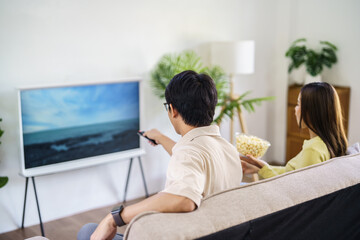 Asian family Watching smart TV together and using remote controller Hand holding popcorn at home with the remote control movie or TV series spending time at home