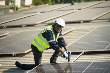 Obraz na płótnie Canvas Well-equipped worker in protective clothing working and examining solar panels on a photovoltaic rooftop plant. Concept of maintenance and installation of solar station.