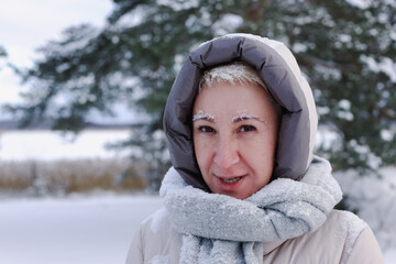 Portrait of happy beautiful elderly senior retired woman in age is playing, having fun with snow outdoors in forest or park at winter cold day, smiling, enjoy weather