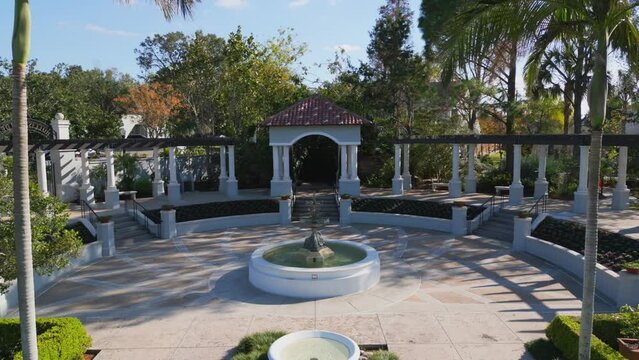 Backward drone shot through opulent and beautiful manicured gardens with fountains running down the middle of the walking path