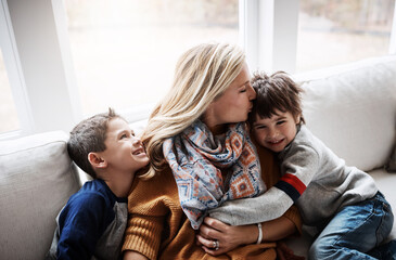 Happy family, hug and kiss from mother to children while together on living room sofa at the house. Woman and kids in lounge for love, care and safety while bonding to relax and spend time at. home