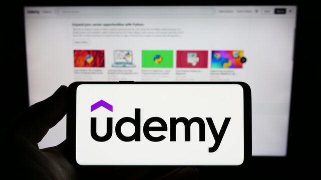Stuttgart, Germany - 01-14-2023: Person holding smartphone with logo of US online education company Udemy Inc. on screen in front of website. Focus on phone display.