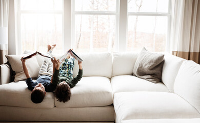 Fun children, bonding and reading books in education, learning or relax studying upside down on house living room or sofa. kids, storytelling and fantasy fairytale novel in creative home inspiration