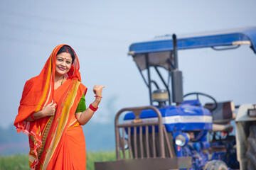 Indian rural woman standing near new tractor and giving happy expression.