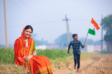 Indian little boy running and waving national flag and his mother setting at agriculture field.