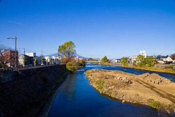 Fototapeta premium Mount Iwate scene with buildings and promenade at Katakami river in Morioka city, Iwate prefecture, Tohoku, Japan.