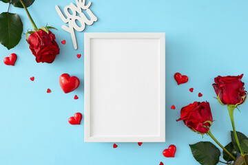 Women day concept. Top view composition made of red roses, hearts, inscription love you on pastel blue background and vertical frame in the middle. 8-march holiday card idea.