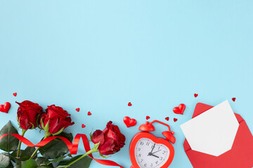 Women day concept. Flat lay photo of open envelope with white card, red flowers, alarm clock and red hearts on pastel blue background with copy space. 8-march holiday card idea.