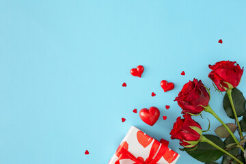 Women day concept. Flat lay photo of red flowers, gift box and red hearts on pastel blue background with copy space. 8-march holiday card idea.