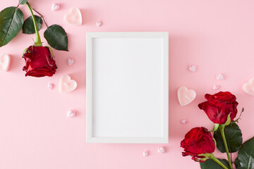 Mother's day concept. Flat lay composition made of red roses and heart shaped candles on pastel pink background and vertical frame in the middle. 8-march holiday card idea.