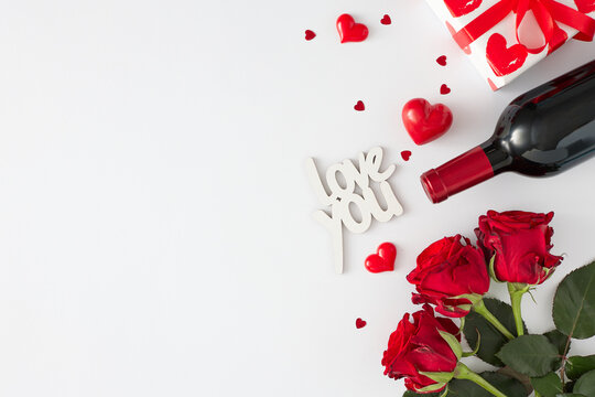 Women day presents concept. Flat lay photo of red roses, wine bottle, gift box, inscription love you and red hearts on white background with copy space. 8-march holiday card idea.