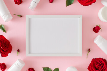 Women's day gift concept. Flat lay photo of cosmetic bottles, red roses with leaves on pastel pink background and white frame in the middle. 8-march holiday card idea.