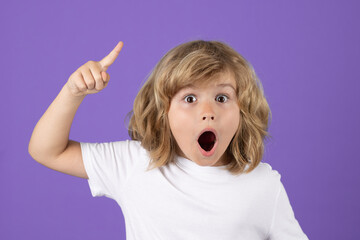 Surprised kid boy pointing up finger on blue background. Shocked kid pointing to copyspace, showing promo offers, points away. Excited emotions, shock, omg and wow expression. - obrazy, fototapety, plakaty