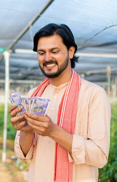 vertical shot of Happy smiling young farmer at greenhouse couting money or currency notes - concept of successful business, agronomy and financial or banking