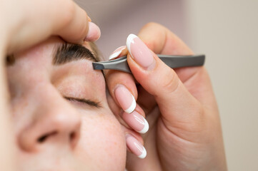 The master makes the client eyebrow correction with tweezers. 