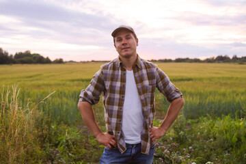 Naklejka na ściany i meble Farmer in front of a sunset agricultural landscape. Man in a countryside field. Country life, food production, farming and country lifestyle concept.
