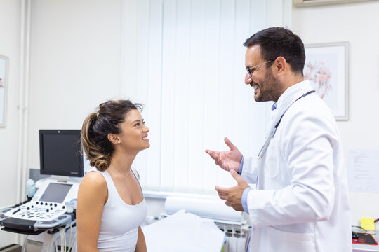 Male doctor consulting female patient at consultation. Professional physician wearing white coat talking to woman at appointment visit in clinic.