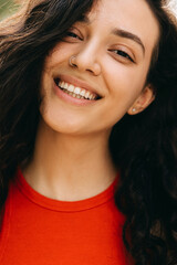 Closeup portrait of a young woman with curly brunette hair, happy, with beautiful smile, looking at camera.