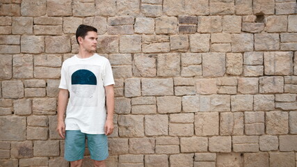A man in a T-shirt in front of a stone wall