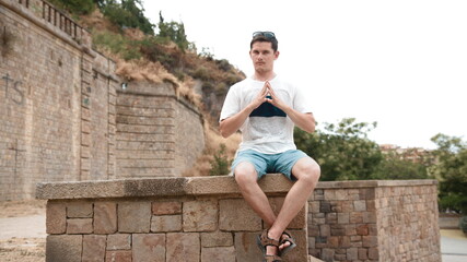 A man in a T-shirt sits on a ledge of an old wall and thinks. Idea for business or creativity