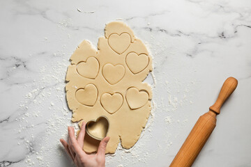 Cutting out heart shaped cookies from rolled out shortbread dough on marble table dusted with flour - 562649580