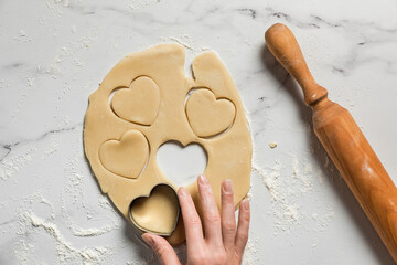 Cutting out heart shaped cookies from rolled out shortbread dough on marble table dusted with flour