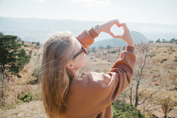 Woman having heart with her hands at sunny day in the forest in Turkey. Trekking concept. 