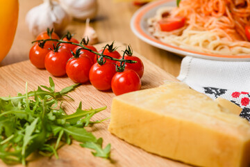 Sprig of cherry tomatoes on the table with garlic, parmesan cheese, arugula leaves and a bowl of pasta.