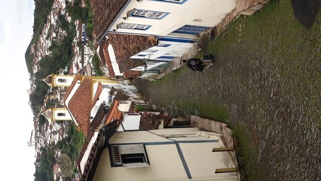 traveler walks down narrow cobbled slope between historic buildings in Ouro Preto, MG, Brazil. VERTICAL