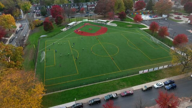 Aerial orbit around soccer team practicing on multi-use field in America during autumn.