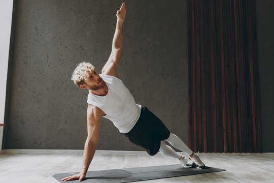 Full Body Side View Young Strong Sporty Sportsman Man Wear White Tank Shirt Black Shorts Doing Side Plank Exercise Pilates With Outstretched Hand Warm Up Training Indoor At Gym. Workout Sport Concept.