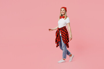 Full body smiling cheerful fun happy cool young woman wear white t-shirt red hat walking going looking camera isolated on plain pastel light pink background studio portrait. People lifestyle concept. - obrazy, fototapety, plakaty
