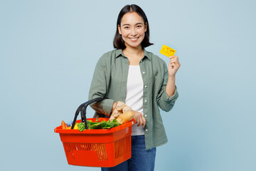 Young cheerful happy woman in casual clothes hold red basket with food products mock up of credit...