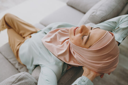 Top view minded young calm muslim woman wear hijab casual clothes sits on sofa couch stay at home flat rest relax spend free spare time in living room indoor. People uae middle eastern islam concept.