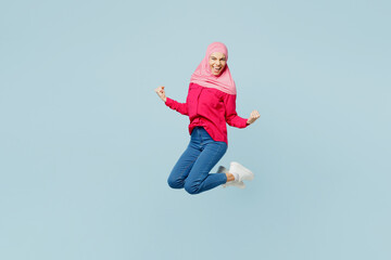 Fototapeta na wymiar Full body side view young arabian asian muslim woman wearing pink abaya hijab jump high do winner gesture isolated on plain pastel light blue cyan background studio portrait People uae islam concept.